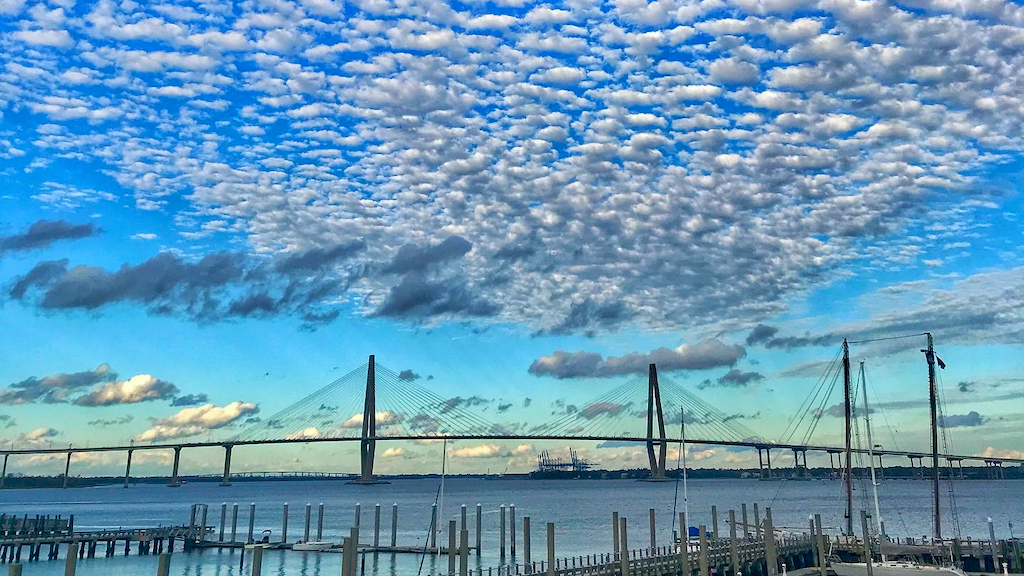 A view of Charleston Harbor from a marina, with the Ravenel Bridge behind and puffy clouds above