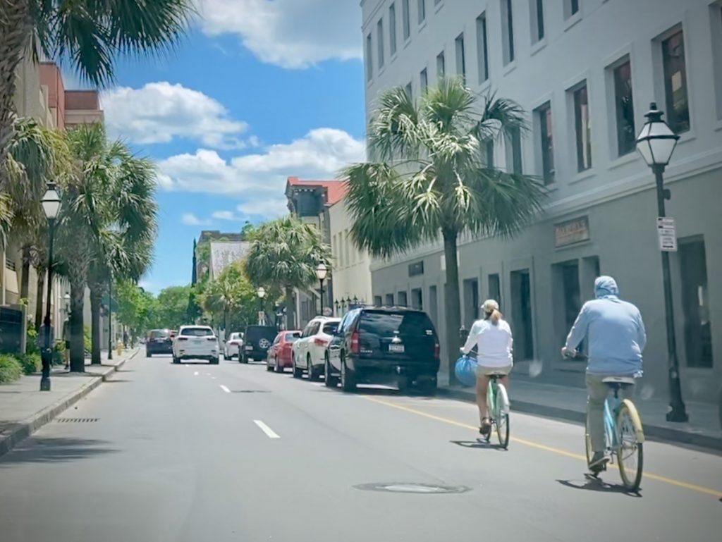 View from a city street between buildings on both sides with two bicyclists riding through the right lane.