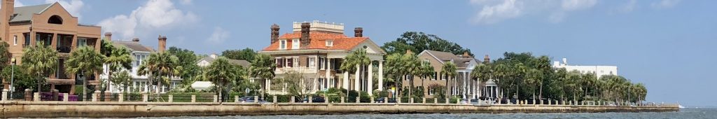 A panoramic view of the High Battery from the vantage point of Charleston Harbor with a row of large homes of many colors.
