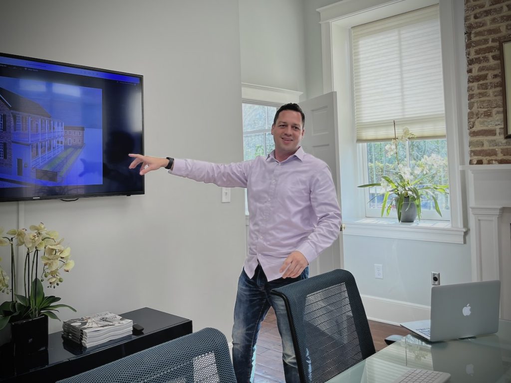 Bryan pointing to a wall mounted screen while speaking in a conference room of an old building