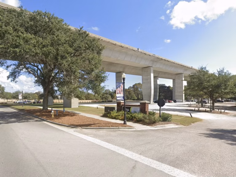 Highway overpass at Interstate 526 in Daniel Island, with concrete pillars and beams, trees along a landscaped roadside, and a bright blue sky.