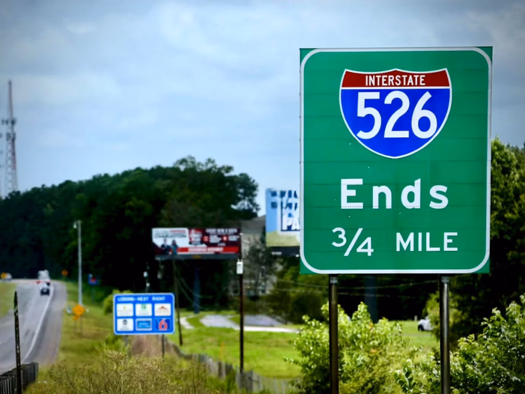 Green Interstate 526 sign showing “Ends” and “3/4 MILE,” with roadside trees and a multi-lane highway in the background.